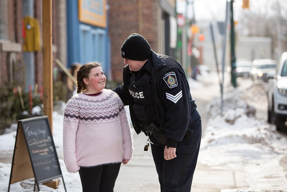 A Peterborough Police officer leans down to speak with a young girl on a winter street