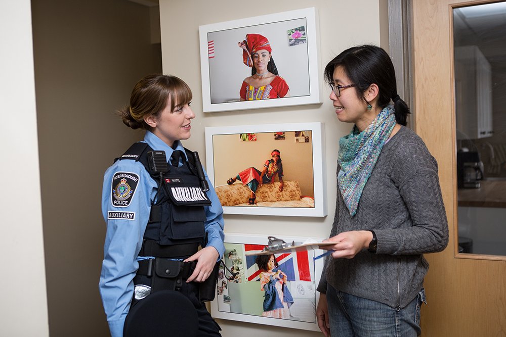 A police officer from the Auxiliary unit has a conversation with a woman in a hallway in front of portraits 