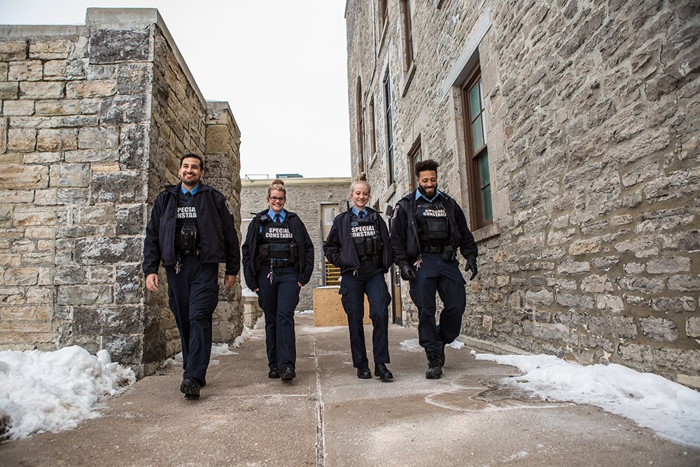 4 special constables walk laughing between 2 stone buildings