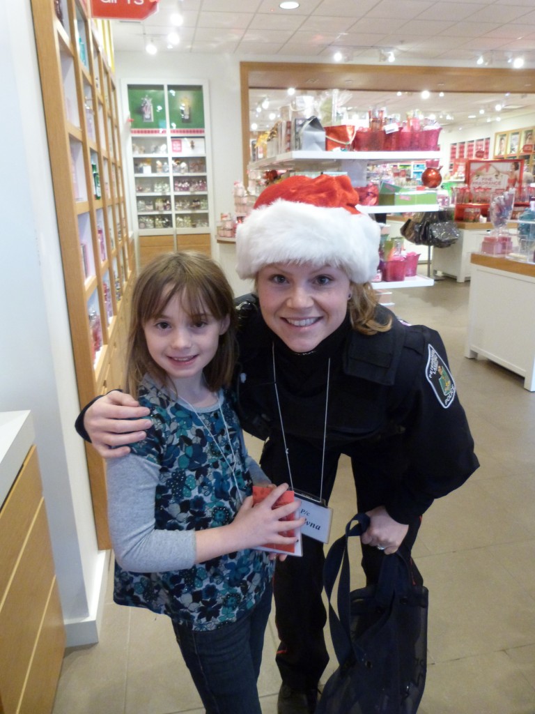 A police officer wearing a santa hat stands with her arm around her child in a store