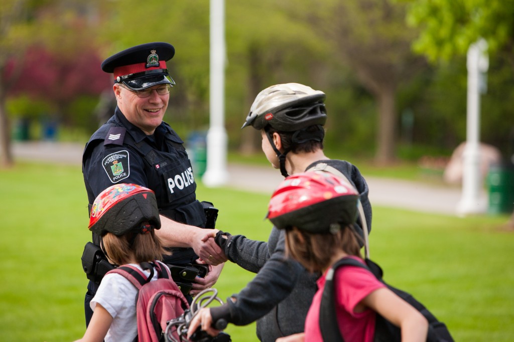 A police officer shakes hands with children who are wearing their bike helmets in a park