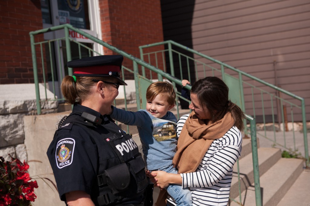 A Peterborough Police officer smiles at a small child that is being held by their mother while the child reaches out to the police officer
