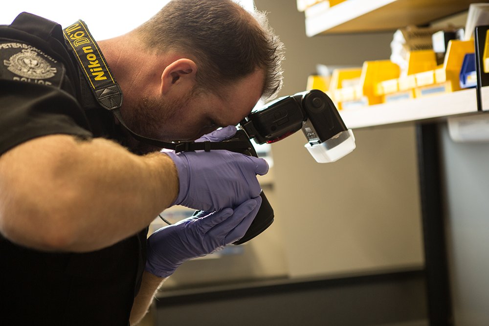 A police officer takes a picture of something outside of the frame in a lab