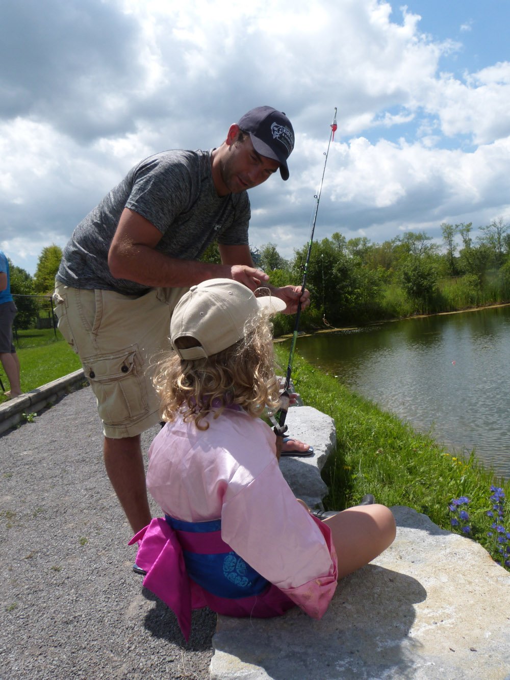 A Peterborough Police Officer showing a fisihing rod to a small child in front of a small lake