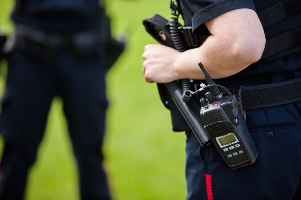 A Peterborough Police Officer rests their hand on the top of their billy club which is holstered beside their radio in their belt. 