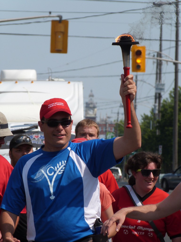 A man in running clothing carries a torch above his head while surrounded by supporters